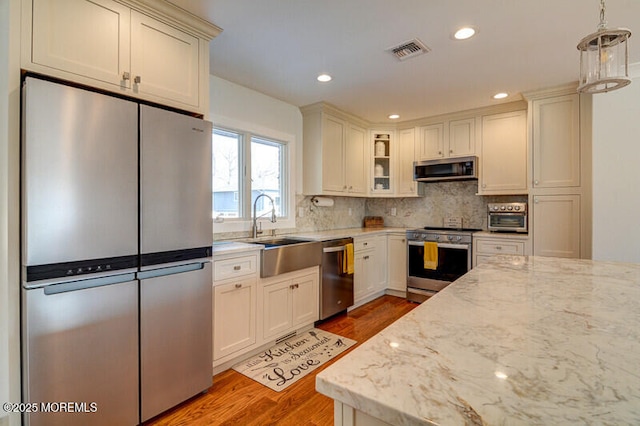 kitchen featuring sink, hanging light fixtures, light stone counters, wood-type flooring, and stainless steel appliances