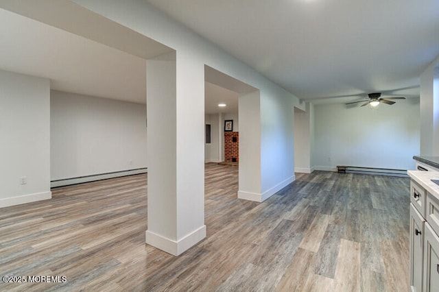 unfurnished living room featuring baseboard heating, ceiling fan, and hardwood / wood-style floors