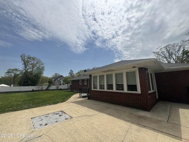 view of property exterior featuring a lawn, a patio area, brick siding, and fence