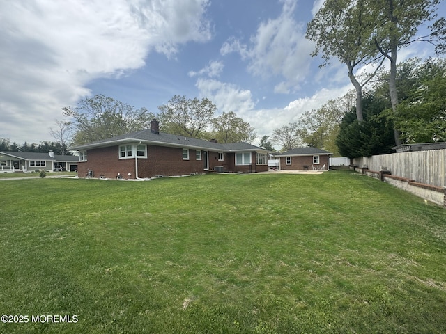 rear view of house featuring a chimney, brick siding, fence, and a lawn