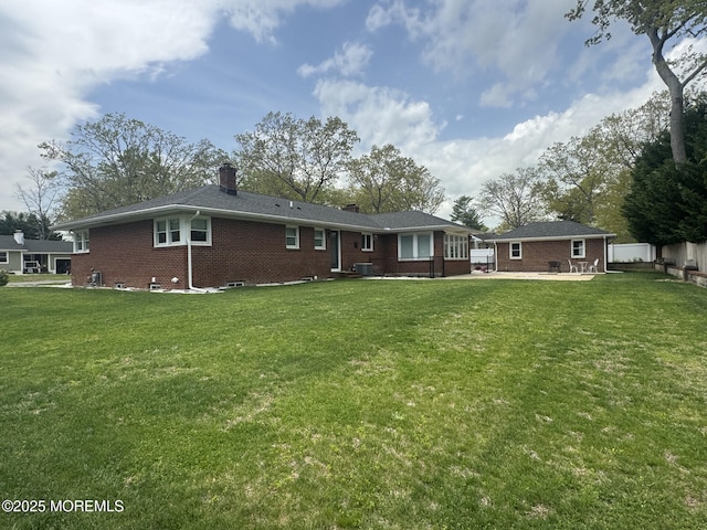 rear view of house featuring a patio, a chimney, brick siding, and a lawn