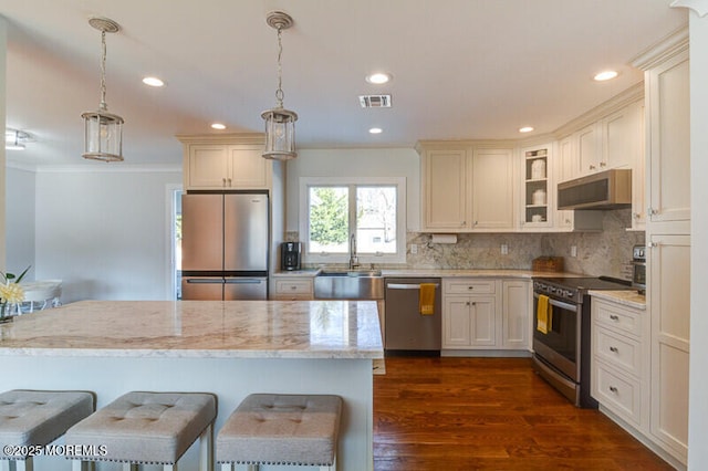 kitchen featuring a sink, visible vents, pendant lighting, glass insert cabinets, and appliances with stainless steel finishes