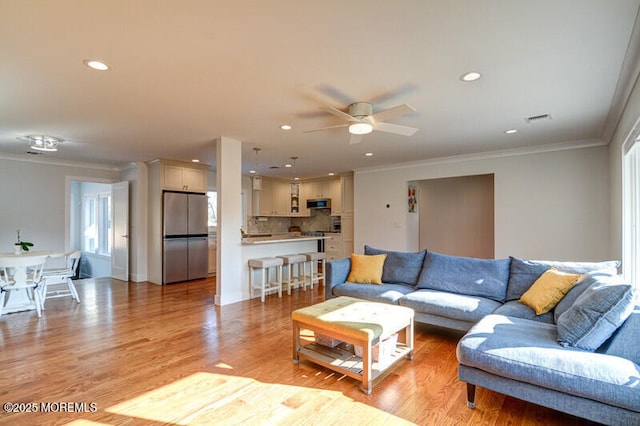 living area with visible vents, ceiling fan, light wood-style floors, ornamental molding, and recessed lighting