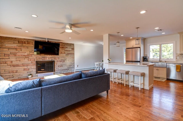 living area featuring light wood-style flooring, a ceiling fan, a fireplace, visible vents, and recessed lighting