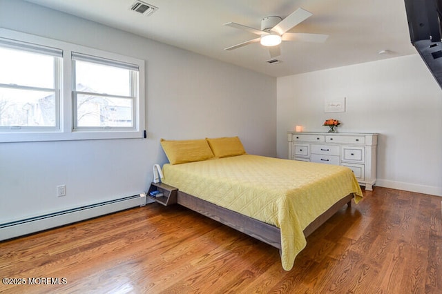 bedroom featuring a baseboard heating unit, ceiling fan, visible vents, and wood finished floors