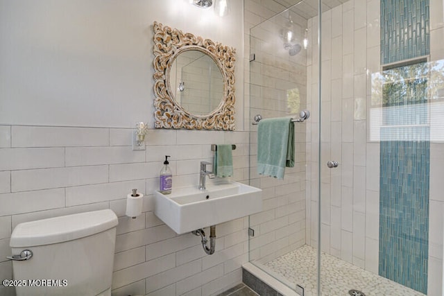 bathroom featuring a stall shower, toilet, a sink, and tile walls