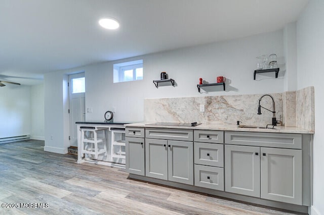kitchen with light wood finished floors, a sink, backsplash, black electric cooktop, and gray cabinetry