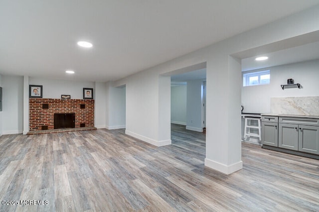 below grade area featuring light wood-type flooring, baseboards, a brick fireplace, and recessed lighting