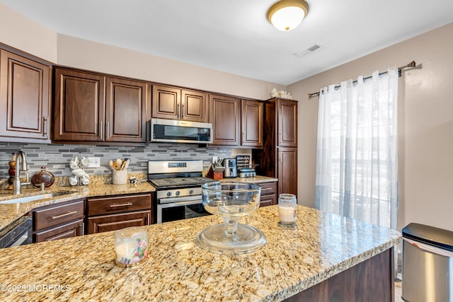 kitchen featuring backsplash, light stone counters, dark brown cabinets, stainless steel appliances, and sink