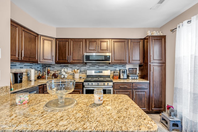 kitchen with dark brown cabinetry, light stone counters, decorative backsplash, and appliances with stainless steel finishes