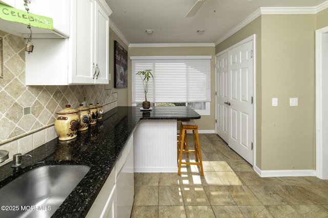 kitchen featuring dark stone countertops, a kitchen bar, decorative backsplash, sink, and white cabinetry