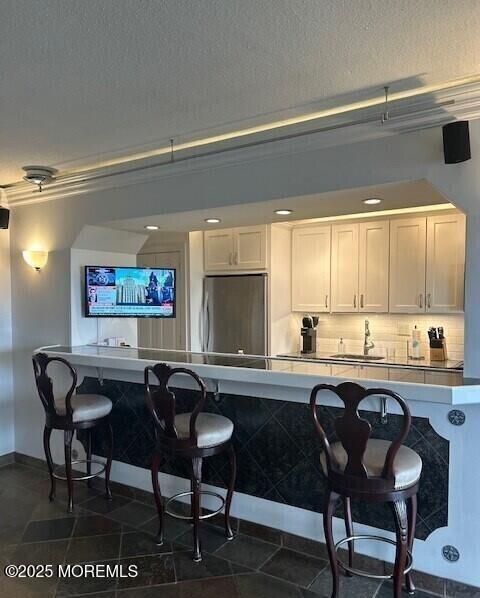 bar featuring sink, white cabinetry, a textured ceiling, decorative backsplash, and stainless steel refrigerator