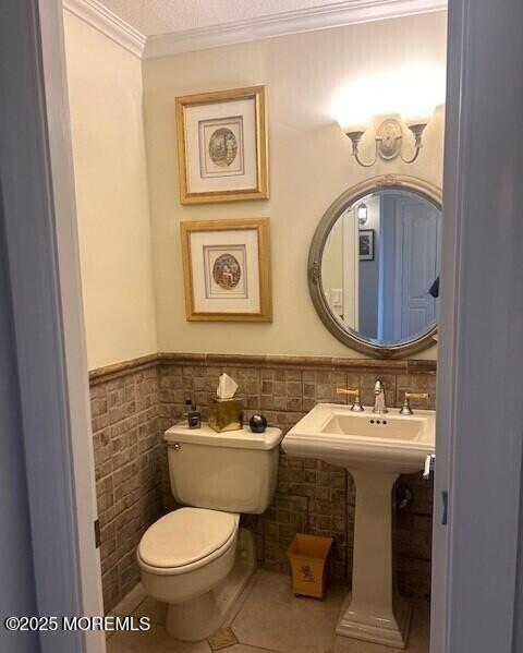 bathroom featuring toilet, a textured ceiling, tile patterned flooring, tile walls, and ornamental molding