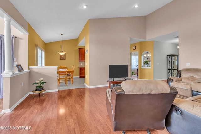 living room featuring light hardwood / wood-style floors, ornate columns, and vaulted ceiling