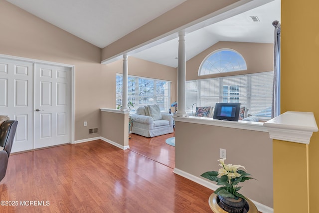 foyer entrance featuring decorative columns, wood-type flooring, and vaulted ceiling