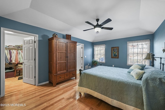 bedroom with light hardwood / wood-style floors, ceiling fan, multiple windows, a tray ceiling, and a walk in closet