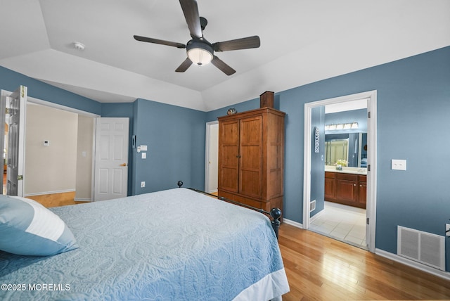 bedroom featuring lofted ceiling, connected bathroom, ceiling fan, light wood-type flooring, and a tray ceiling