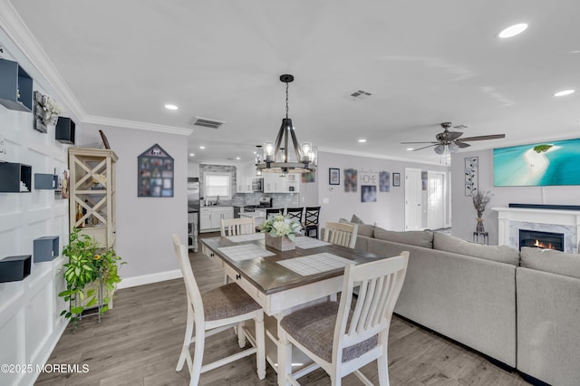 dining area featuring ceiling fan with notable chandelier, light hardwood / wood-style flooring, crown molding, and a premium fireplace