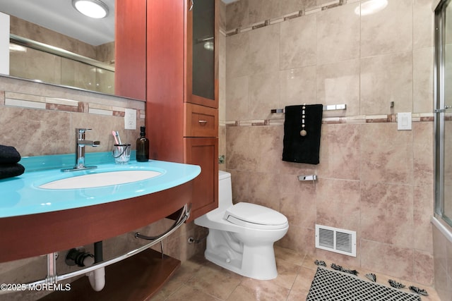 bathroom with visible vents, toilet, tile patterned flooring, a tile shower, and a sink