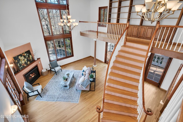 living area with plenty of natural light, wood finished floors, a towering ceiling, and an inviting chandelier