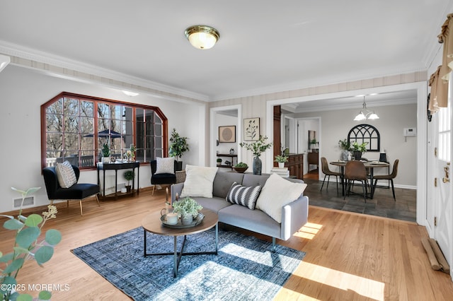 living room featuring ornamental molding, wood finished floors, visible vents, and a notable chandelier