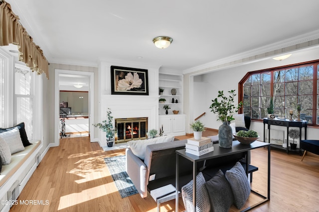 living area with light wood-type flooring, a glass covered fireplace, crown molding, and built in shelves