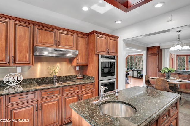 kitchen with brown cabinetry, black electric stovetop, stainless steel double oven, under cabinet range hood, and a sink