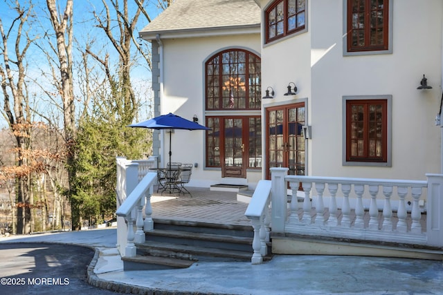 view of exterior entry featuring french doors, roof with shingles, and stucco siding