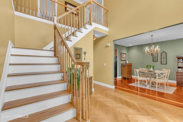 stairs with a towering ceiling, an inviting chandelier, and parquet floors