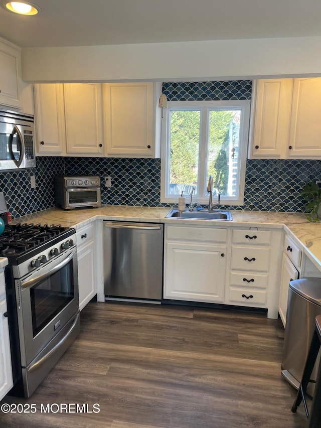 kitchen featuring backsplash, sink, appliances with stainless steel finishes, dark hardwood / wood-style flooring, and white cabinetry