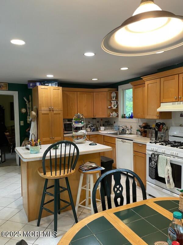 kitchen with white appliances, light tile patterned floors, a breakfast bar, a kitchen island, and backsplash