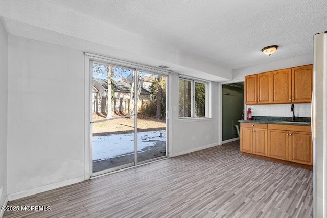 kitchen with sink, fridge, a textured ceiling, light hardwood / wood-style flooring, and backsplash