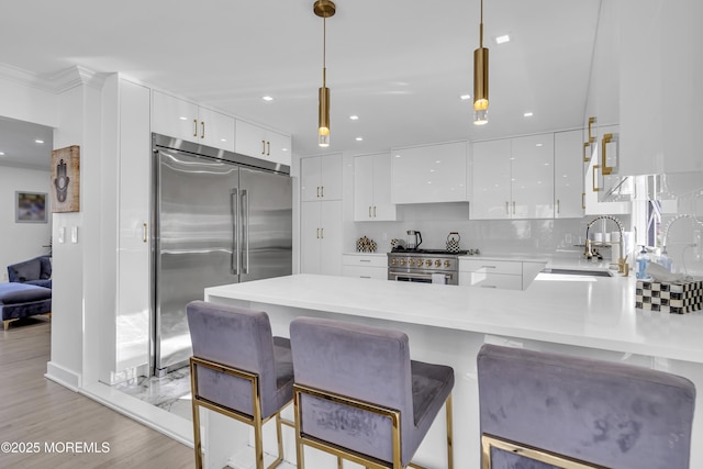 kitchen with white cabinets, decorative light fixtures, kitchen peninsula, and high end appliances