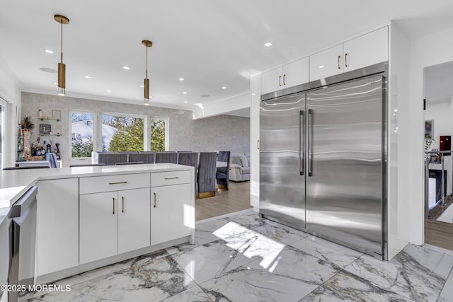 kitchen with white cabinetry, crown molding, stainless steel built in refrigerator, and hanging light fixtures