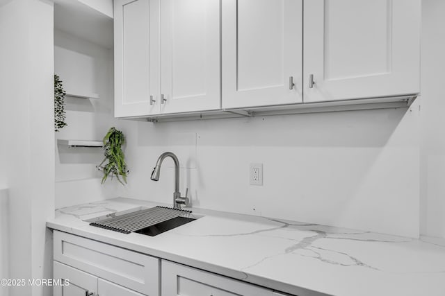 kitchen featuring light stone counters, white cabinetry, and sink