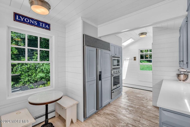 kitchen featuring built in appliances, vaulted ceiling, gray cabinets, baseboard heating, and plenty of natural light