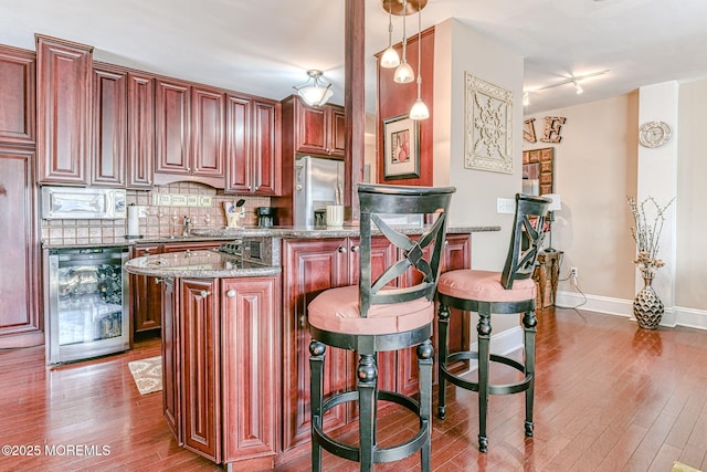 kitchen featuring stainless steel refrigerator with ice dispenser, tasteful backsplash, light stone counters, wine cooler, and hanging light fixtures