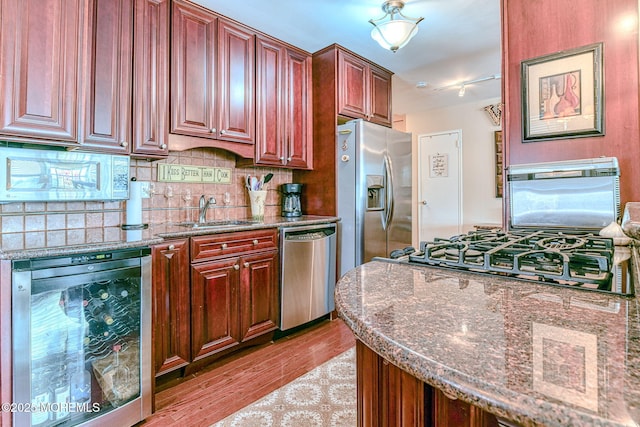 kitchen with dark stone counters, sink, light hardwood / wood-style floors, stainless steel appliances, and beverage cooler