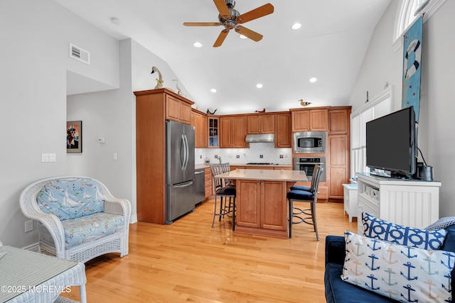 kitchen with a center island, light wood-type flooring, tasteful backsplash, a breakfast bar, and appliances with stainless steel finishes