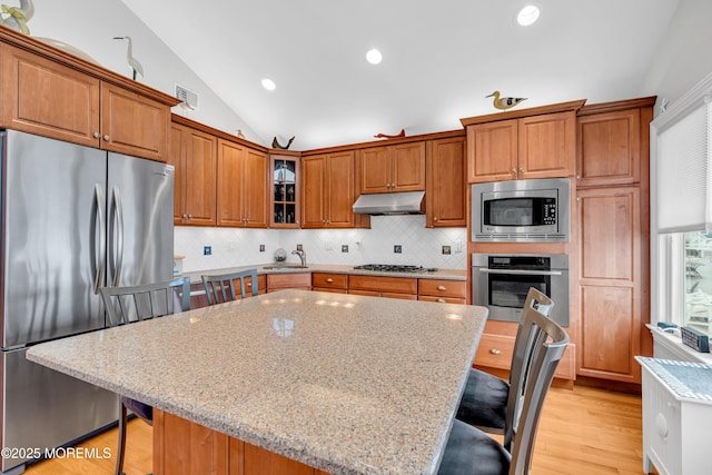 kitchen featuring stainless steel appliances, a kitchen island, a kitchen breakfast bar, and light stone countertops