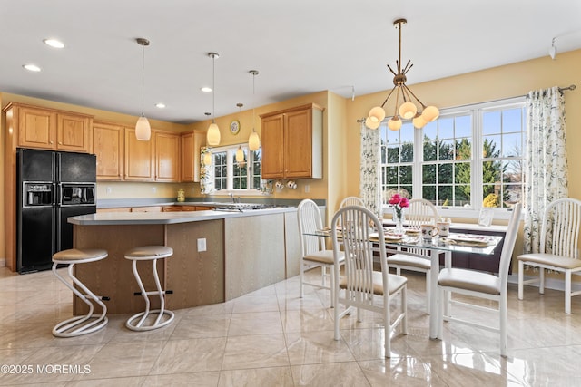 kitchen with black fridge with ice dispenser, a center island, hanging light fixtures, an inviting chandelier, and a breakfast bar area