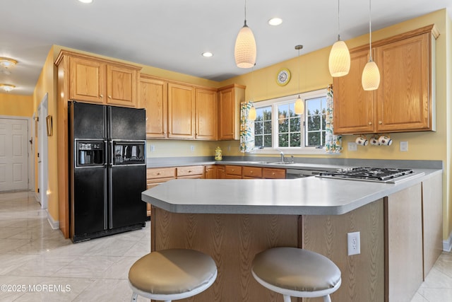 kitchen with black fridge, stainless steel gas stovetop, pendant lighting, a kitchen bar, and sink