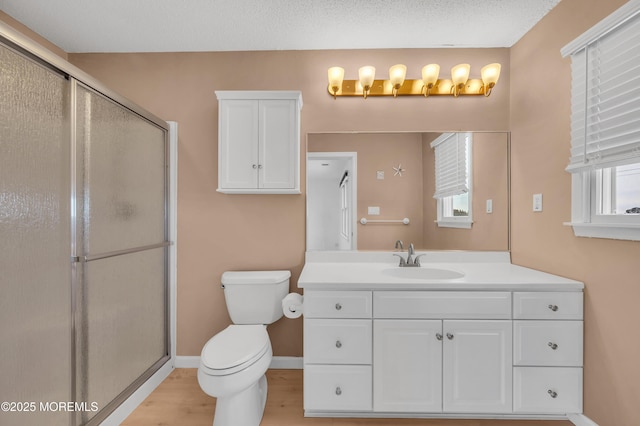 bathroom featuring a textured ceiling, a shower with door, toilet, and vanity