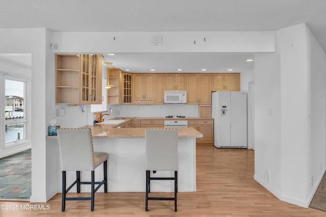 kitchen with a kitchen breakfast bar, kitchen peninsula, light brown cabinetry, sink, and white appliances