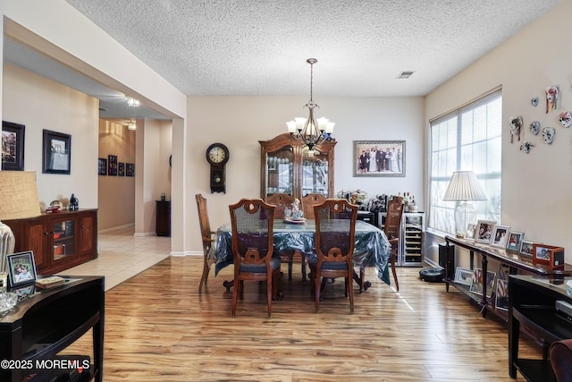 dining area with a textured ceiling, light wood-type flooring, and a notable chandelier