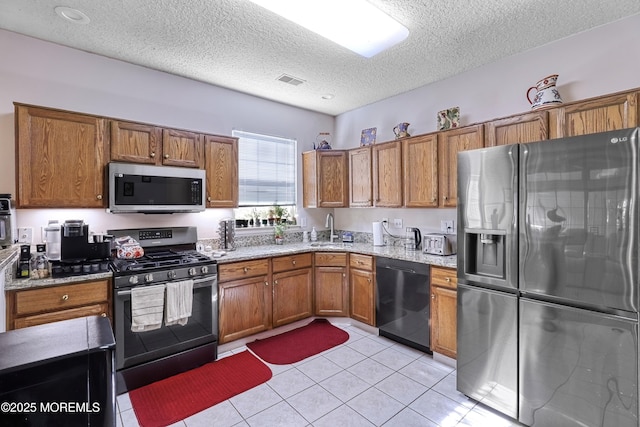 kitchen featuring appliances with stainless steel finishes, light tile patterned floors, light stone counters, a textured ceiling, and sink