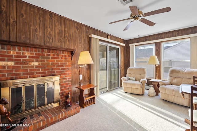 living room with carpet, ceiling fan, wooden walls, a baseboard radiator, and a fireplace