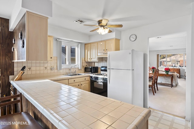 kitchen featuring tile countertops, gas range, white fridge, and sink