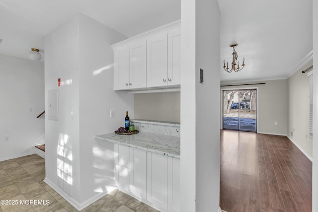 kitchen featuring a notable chandelier, white cabinetry, ornamental molding, and light stone countertops