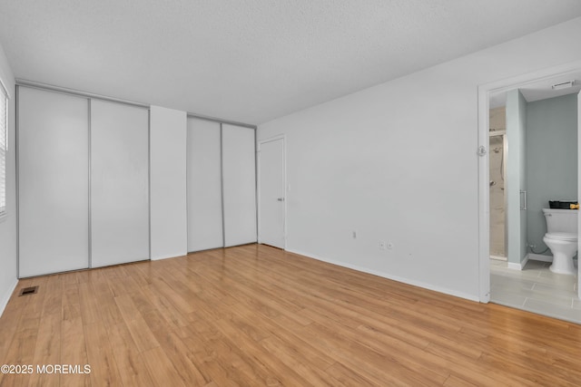 unfurnished bedroom featuring a textured ceiling, multiple closets, light hardwood / wood-style floors, and connected bathroom